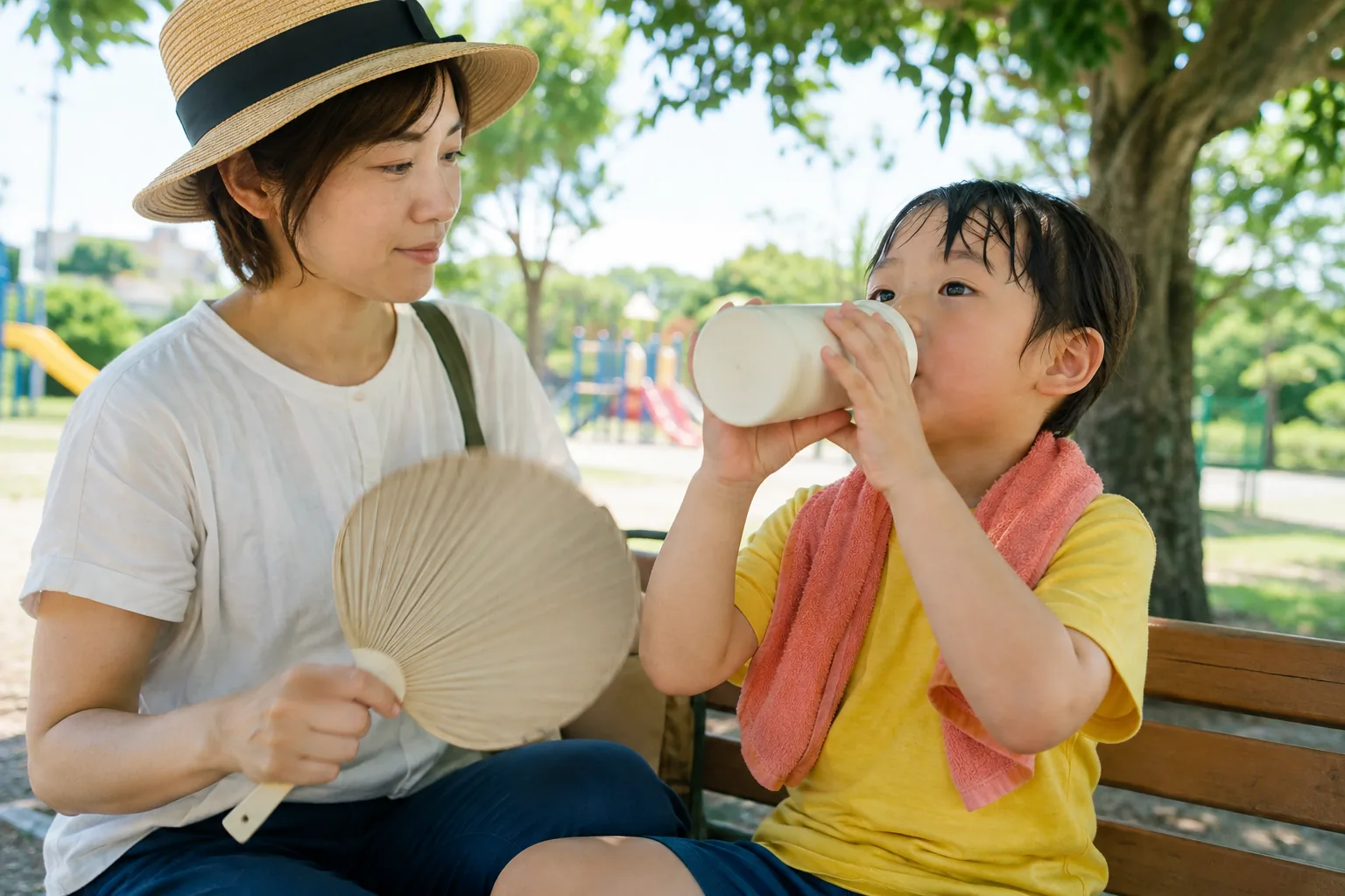 木陰のベンチで水分補給する子どもと見守る保護者